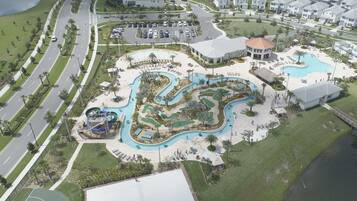 An aerial view of a residential area with a large swimming pool, a golf course, and a basketball court.