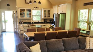 Amplia sala de estar con un sofá seccional grande, una mesa de comedor con sillas y una cocina con armarios blancos y un refrigerador verde.