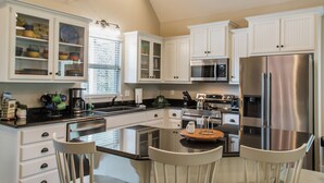 Una cocina moderna con armarios blancos, electrodomésticos de acero inoxidable y una isla central con taburetes.