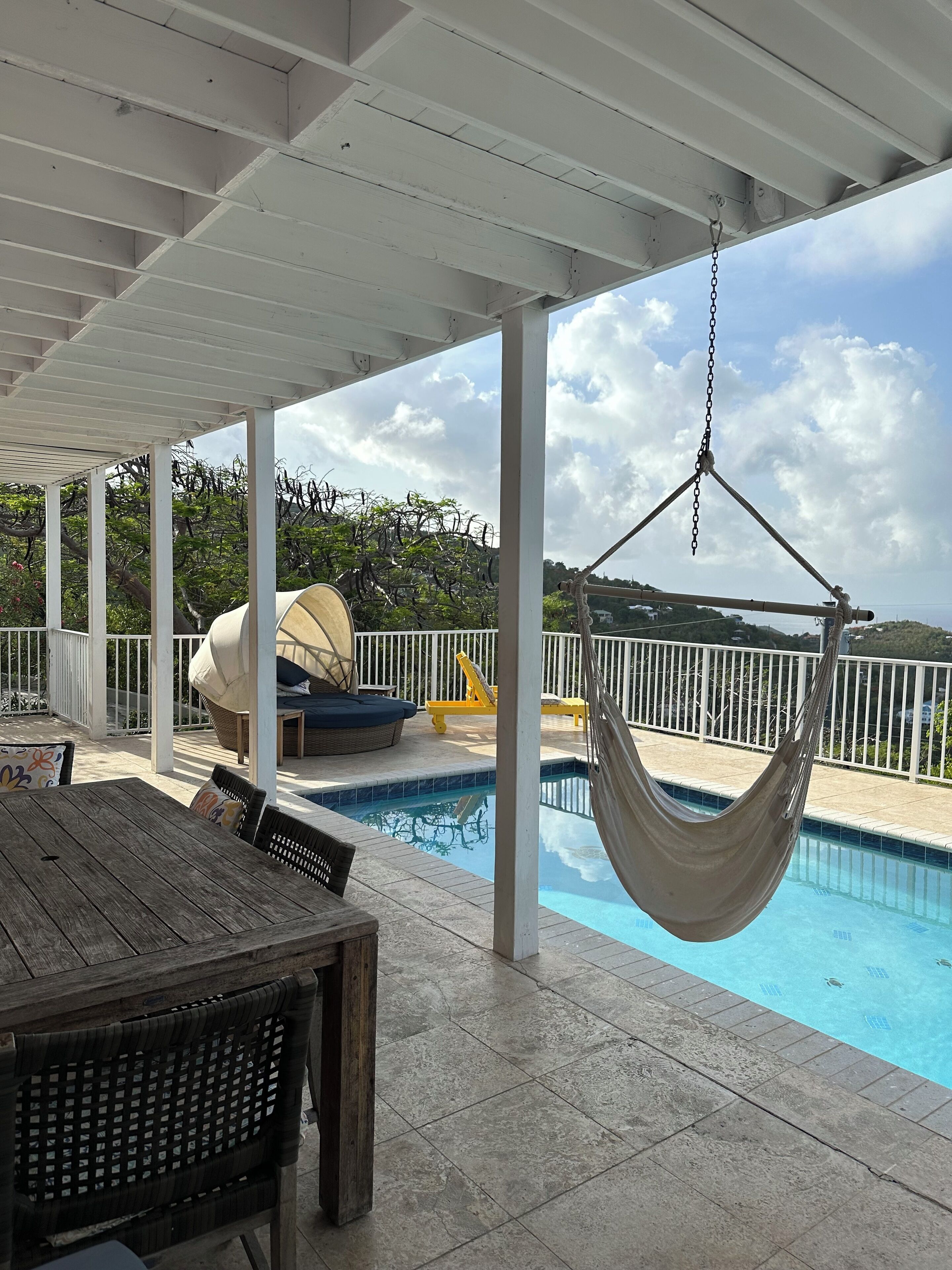 Ein überdachter Außenbereich mit Pool, einer Hängematte und einem Tisch mit Stühlen.