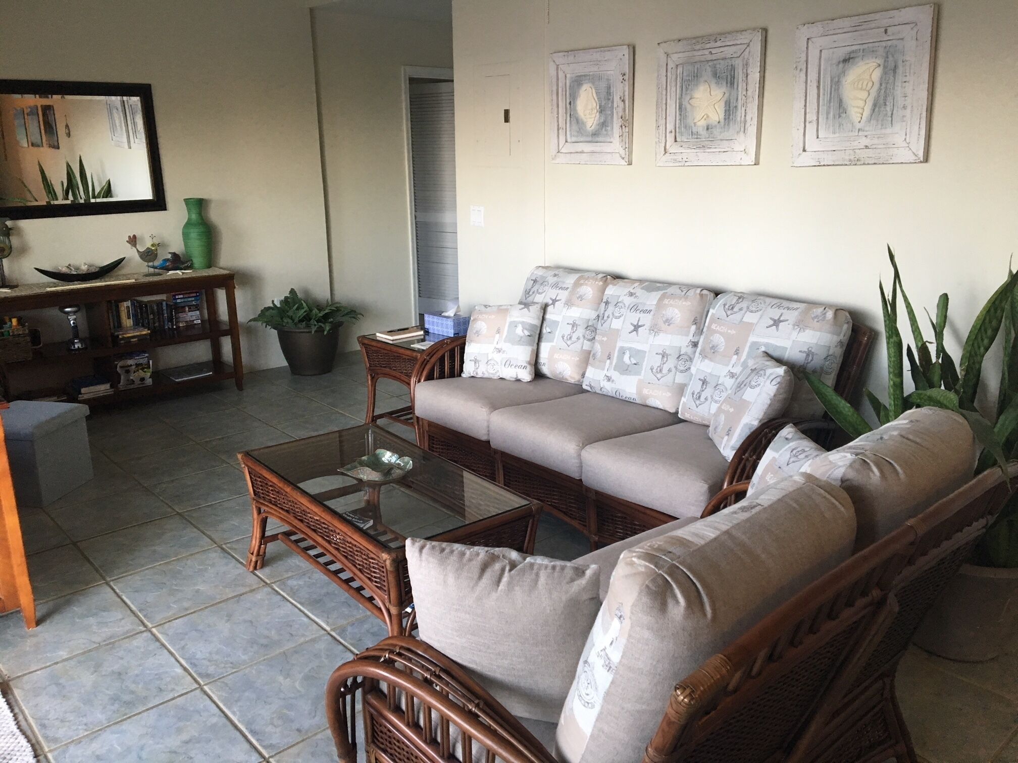 A living room with a sofa, coffee table, and side table. There are framed pictures on the wall, a mirror, and a potted plant.