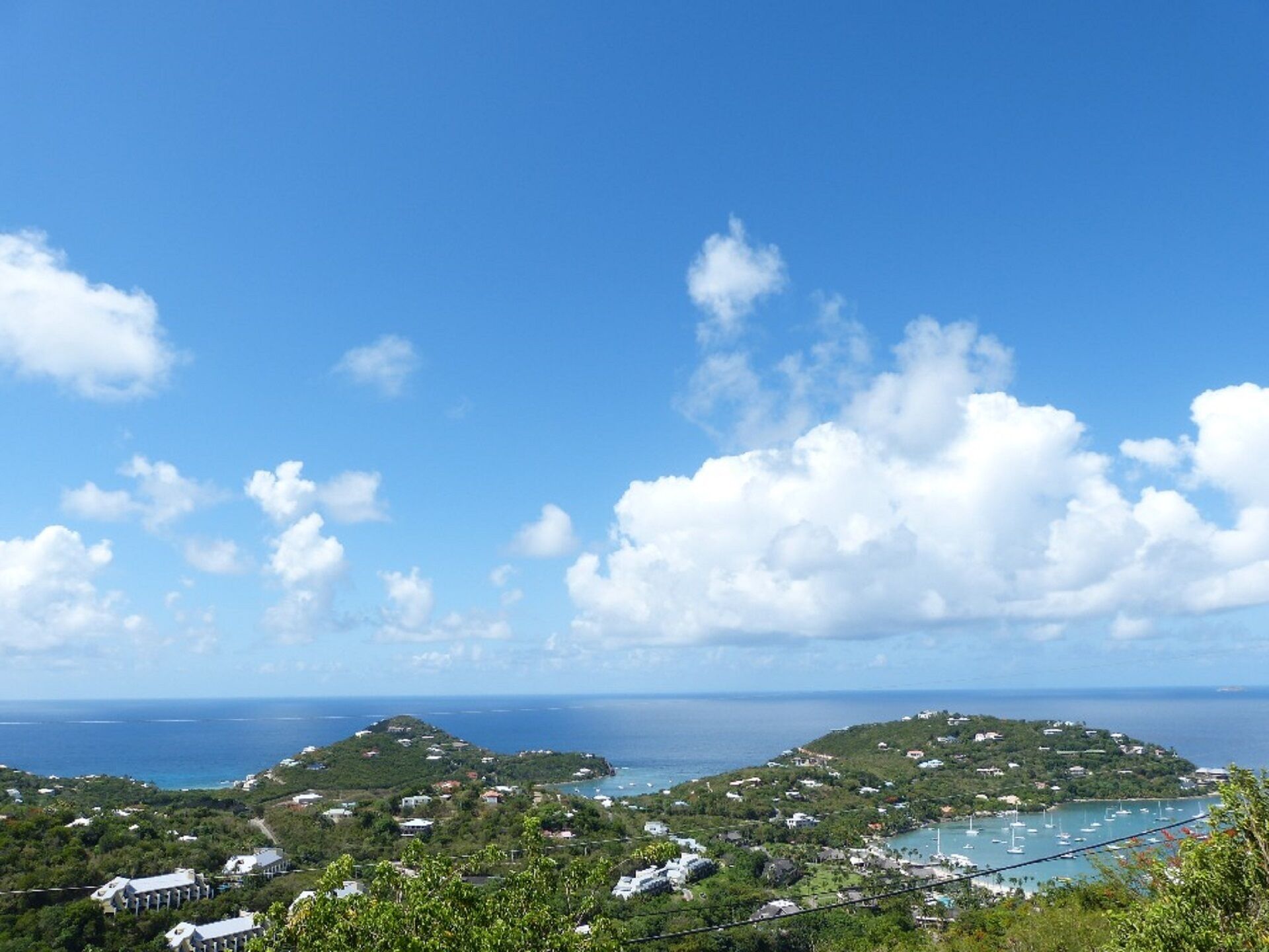 A coastal landscape with lush greenery, a clear blue sky, and a view of the sea.