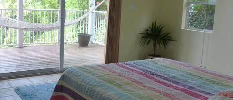 Un dormitorio con una cama grande, una planta en maceta, una hamaca en una terraza al aire libre y vistas a la vegetación.