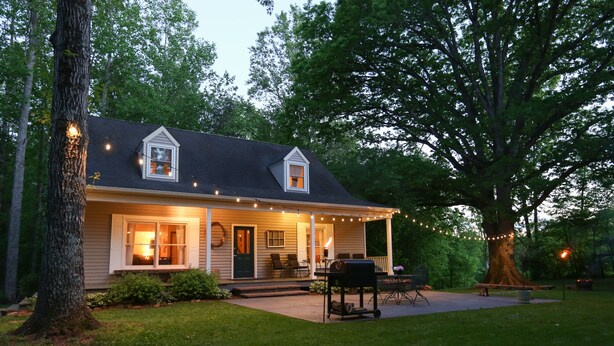 A house with a porch, string lights, a grill, and a tree.
