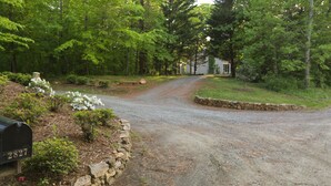 A gravel driveway leading to a house surrounded by lush greenery and a stone wall.