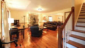 A spacious living room with a stone fireplace, leather sofa, dining area, and a staircase.