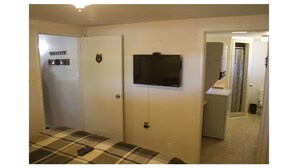 Hotellihuone, jossa on ruutukuviollinen peitto sängyllä, seinälle asennettu televisio ja ovi, jossa on tervetulotoivotus.