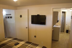 A hotel room with a plaid bedspread, a television mounted on the wall, and a door with a welcome sign.