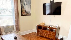A living room with a wooden coffee table, leather sofa, and a TV mounted on the wall. - 1st Base Apt 1 - All Star Baseball Rentals (Oneonta)