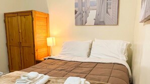 A neatly made bed with a brown bedspread and two folded white towels on the foot of the bed. There is a wooden wardrobe to the left and a painting on the wall above the bed. - 1st Base Apt 1 - All Star Baseball Rentals (Oneonta)