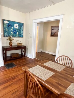 A dining area with a wooden table and chairs, a vase with flowers, and a painting on the wall. - 1st Base Apt 1 - All Star Baseball Rentals (Oneonta)