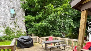 A wooden deck with picnic tables and chairs, surrounded by lush green trees. - 1st Base Apt 1 - All Star Baseball Rentals (Oneonta)
