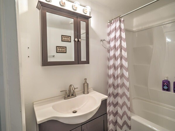 Une salle de bain avec un lavabo blanc, un miroir avec éclairage, un rideau de douche et des articles de toilette accrochés au mur.