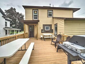 A wooden deck with picnic tables and chairs, a grill, and a building with a door and windows. - 1st Base Apt 1 - All Star Baseball Rentals (Oneonta)