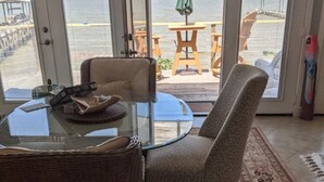 A dining area with a glass table, wicker chairs, and a view of the ocean through large glass doors. - Waterfront Suite on shared property w/ 275' fishing pier and private hot tub (Bacliff)