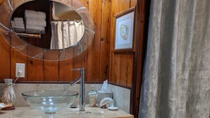 A wooden bathroom vanity with a glass bowl sink, a mirror, and a framed picture on the wall. - Waterfront Suite on shared property w/ 275' fishing pier and private hot tub (Bacliff)