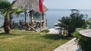 A wooden deck with a thatched umbrella, a flag, and a view of the sea. - Waterfront Suite on shared property w/ 275' fishing pier and private hot tub (Bacliff)