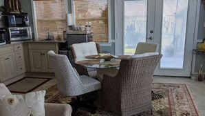 A living room with a sofa, a dining table with chairs, a kitchen area with appliances, and a large window with blinds. - Waterfront Suite on shared property w/ 275' fishing pier and private hot tub (Bacliff)