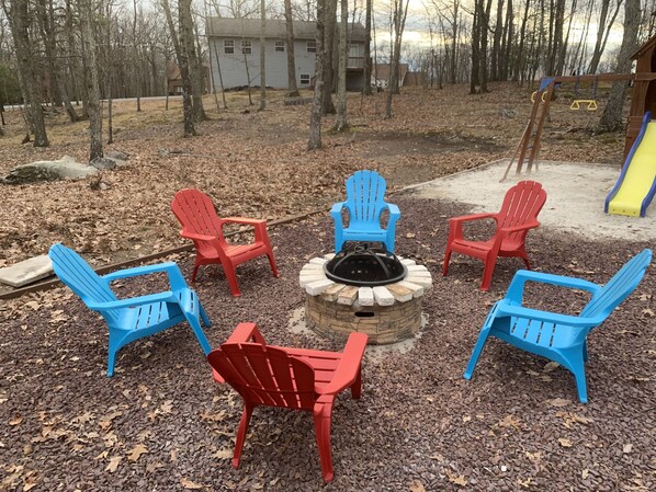 Un aménagement circulaire avec des sièges disposés autour d’un foyer, agrémenté de fauteuils Adirondack rouges et bleus.