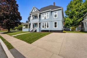 A two-story residential house with a front porch, a driveway, and a well-maintained lawn. - 2nd Base Apt 1 - All Star Baseball Rentals (Oneonta)