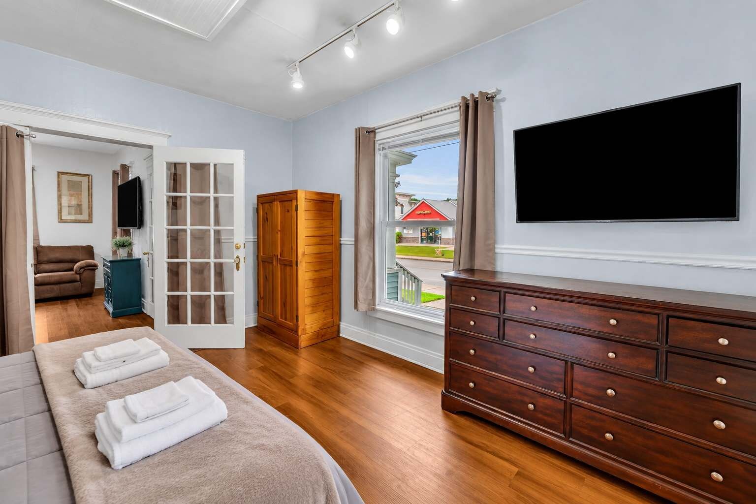 Quarto com cama, cômoda, televisão e vista para o exterior.