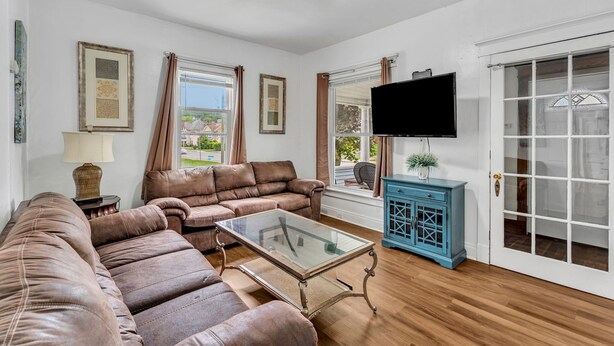 A living room with a brown leather sofa, a glass coffee table, a blue cabinet, and a TV on the wall. - 2nd Base Apt 1 - All Star Baseball Rentals (Oneonta)