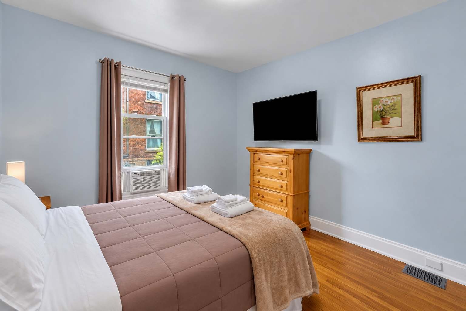A bedroom with a bed, a dresser, a television, and a window with curtains.