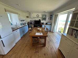 A kitchen with wooden flooring, a dining table, and a view of the outdoors through a window.