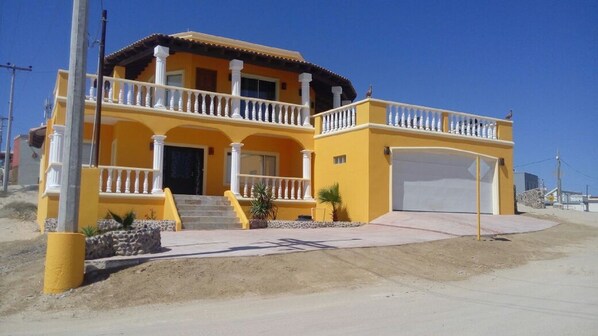 Una casa amarilla de dos pisos con balcón, garaje y un pequeño jardín.