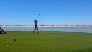 En golfbane med klar himmel og et vandareal i baggrunden.