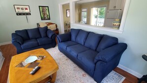 Un soggiorno con due divani blu, un tavolino in legno e una cucina visibile attraverso un'apertura.