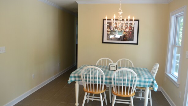 A dining area with a table set for four, white chairs, a chandelier, and a framed picture on the wall.