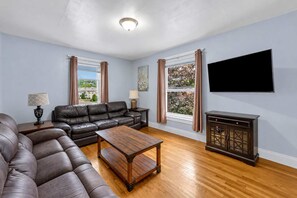A living room with a leather sofa, wooden coffee table, and a TV mounted on the wall. - 2nd Base Apt 2 - All Star Baseball Rentals (Oneonta)