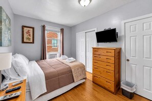 A bedroom with a bed, a dresser, a television, and a window with curtains. - 2nd Base Apt 2 - All Star Baseball Rentals (Oneonta)