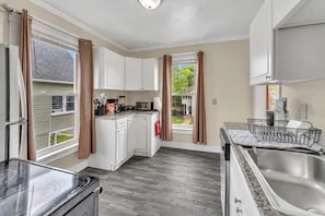 A compact kitchen with white cabinets, a stainless steel sink, and a dish rack. - 2nd Base Apt 2 - All Star Baseball Rentals (Oneonta)