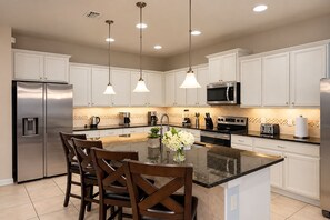 Una cocina moderna con armarios blancos, electrodomésticos de acero inoxidable y una isla central con asientos.