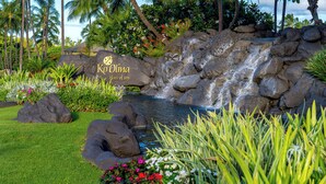 Um jardim tropical com uma cascata, uma placa com a inscrição 'Ko Olina Place of Joy' e vegetação exuberante.