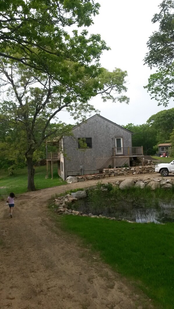 A rustic cabin with a stone foundation, a wooden deck, and a small pond in front.