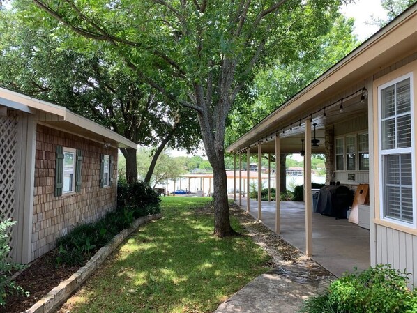 A covered outdoor area with a tree, a brick building, and a covered porch.