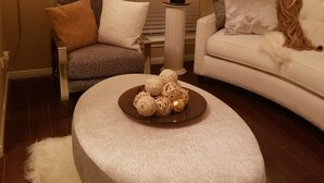 Una sala acogedora con un reposapiés redondo, un sillón estampado y un sofá blanco.