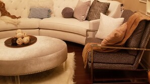 Una sala de estar con un sofá modular, un otoman redondo, un sillón estampado y una escalera con barandilla de madera.