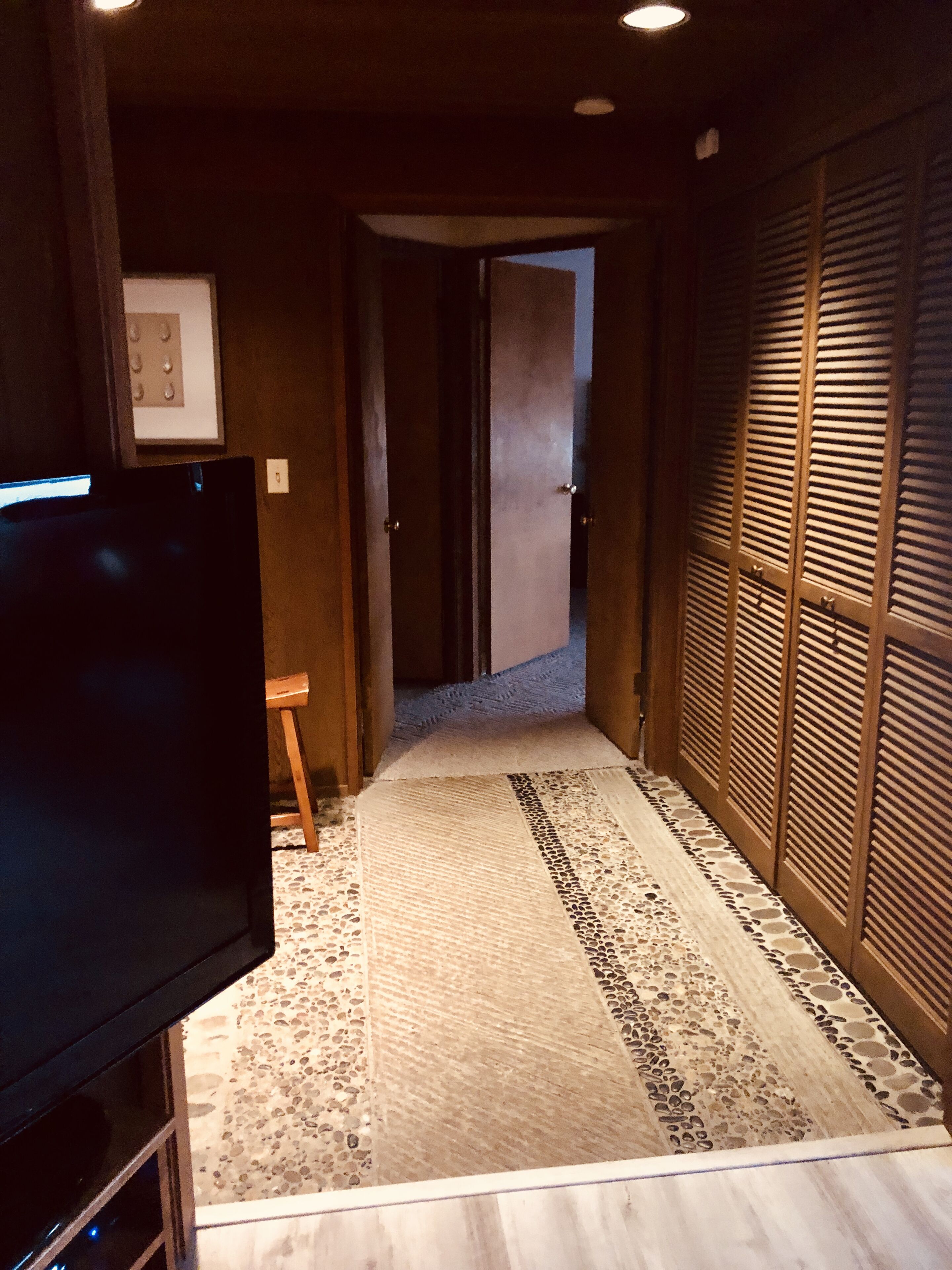 A hallway with a wooden floor, a television on the left, and a sliding door on the right.