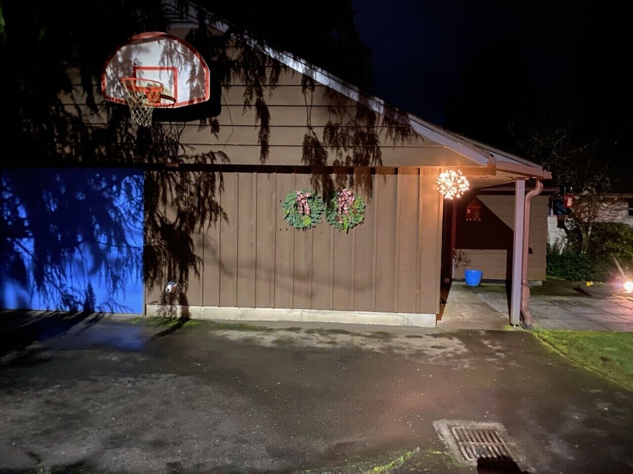 A garage with a basketball hoop, a covered porch, and a decorative wreath on the wall.
