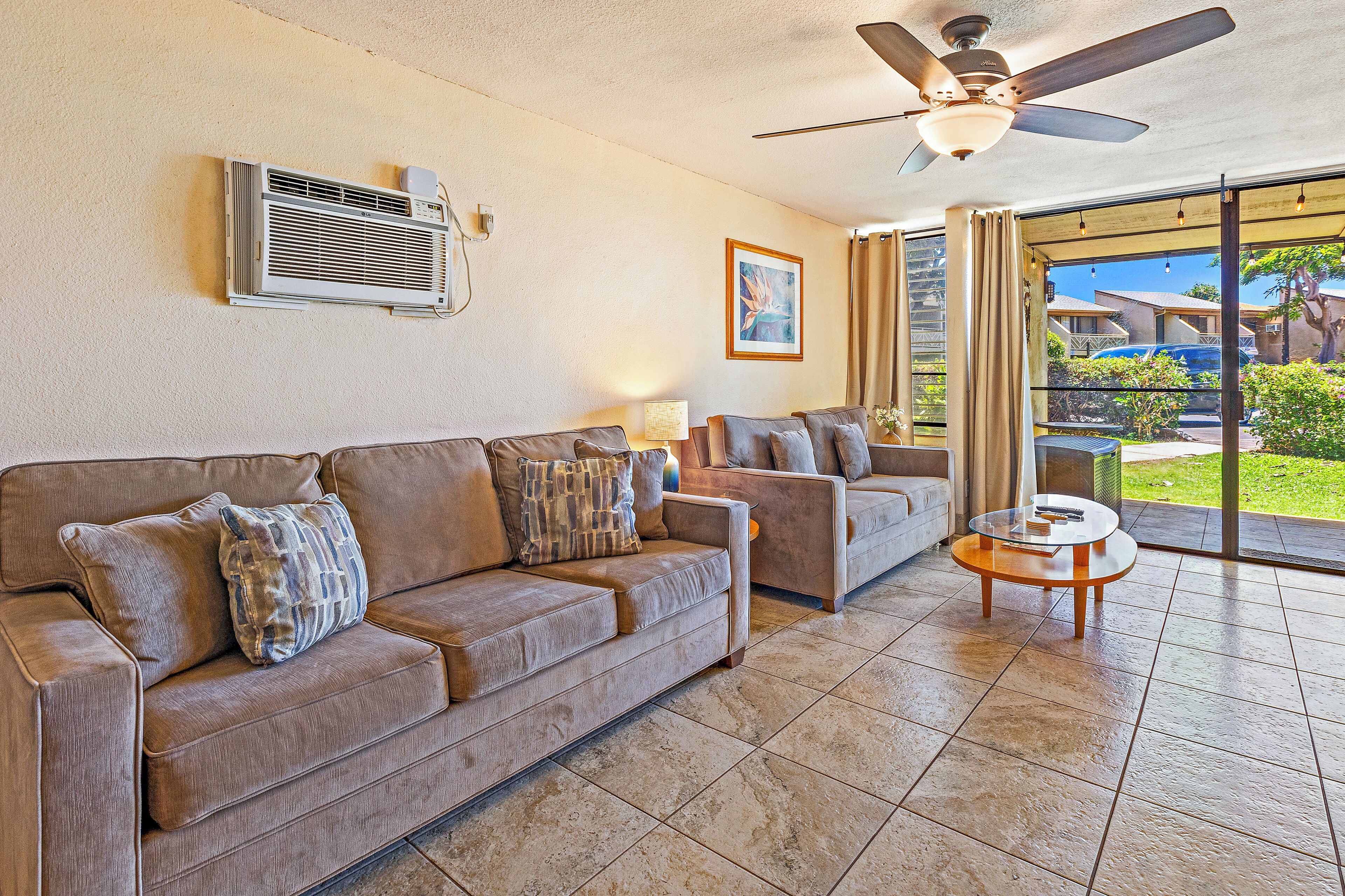 A living room with a beige sofa, a smaller sofa, a glass coffee table, and a ceiling fan.