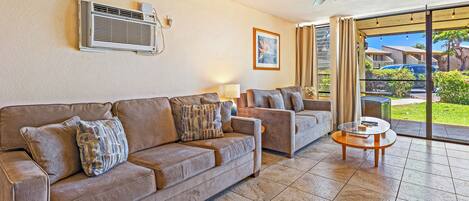 A living room with a beige sofa, a smaller sofa, a glass coffee table, and a ceiling fan.