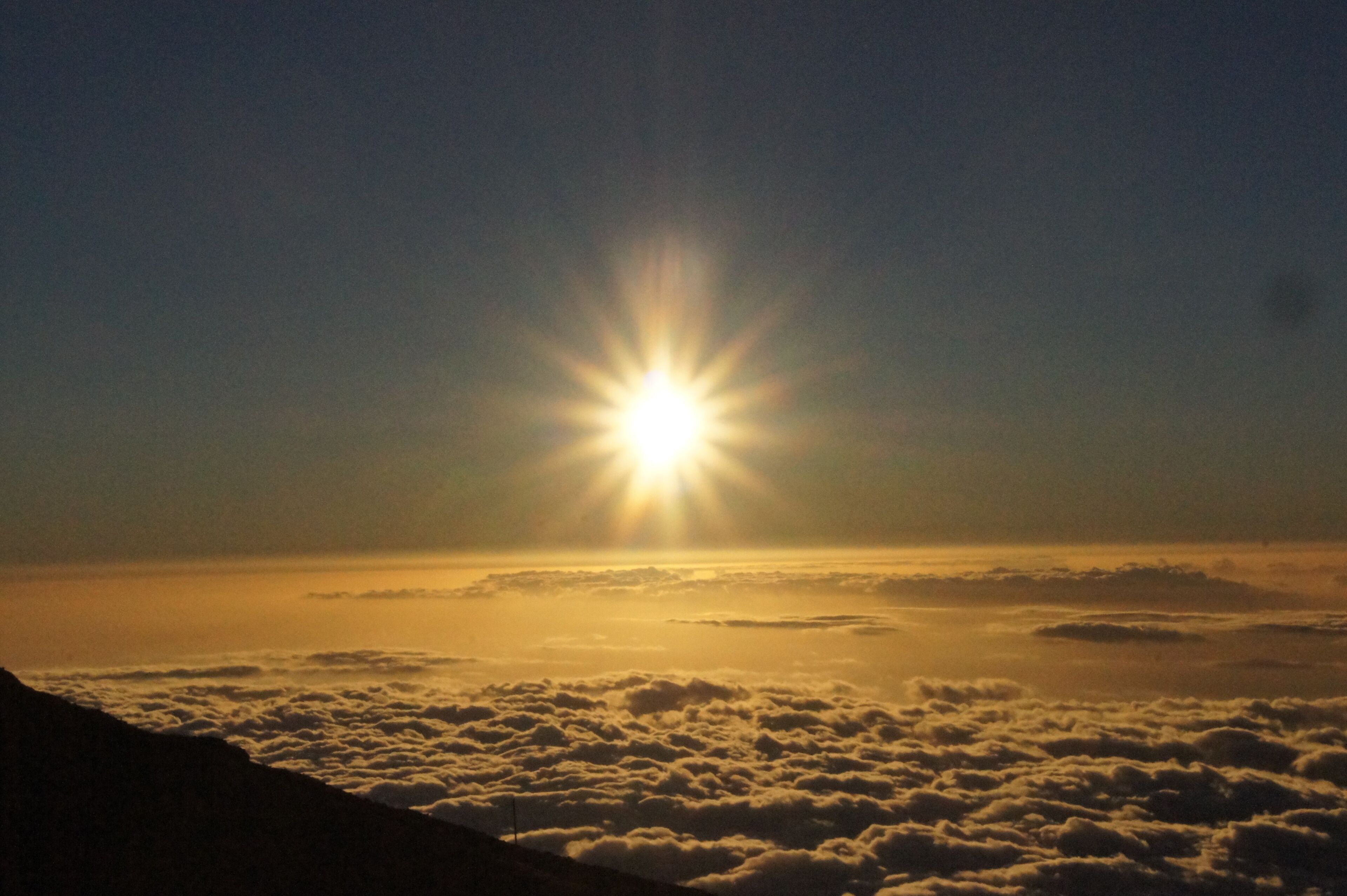 Un lever de soleil sur un paysage montagneux, avec des nuages en contrebas.