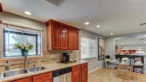 Una cocina moderna con armarios de madera, electrodomésticos de acero inoxidable y un comedor con sillas transparentes.