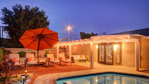 Un área junto a la piscina con sillones de descanso, una sombrilla y luces colgantes.