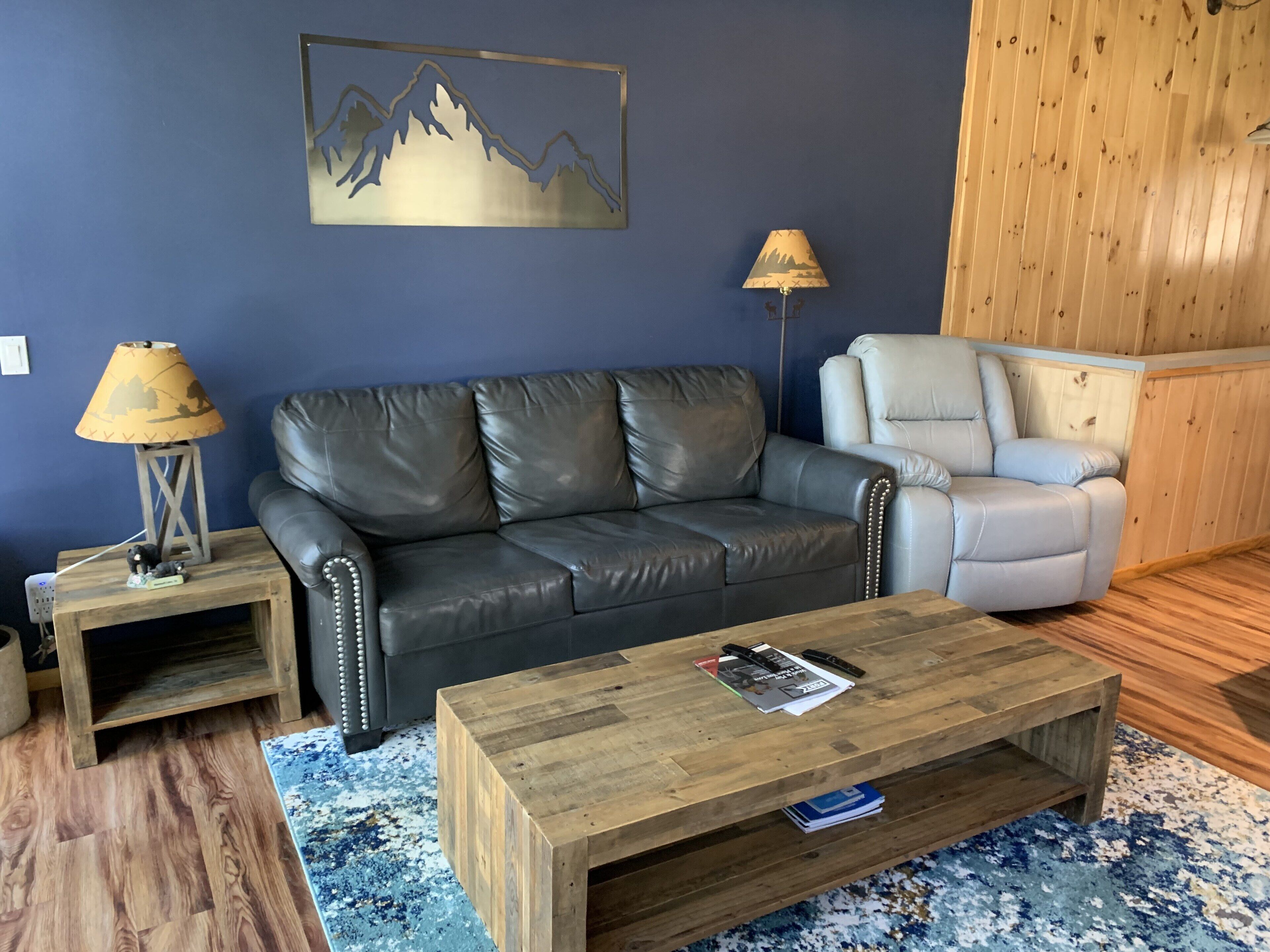 Ein Wohnzimmer mit einem dunkelbraunen Ledersofa, einem hellgrauen Sessel, einem Holztisch und zwei Stehlampen.