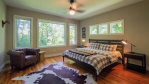 Ein Schlafzimmer mit Bett, Stuhl, Teppich und großen Fenstern.